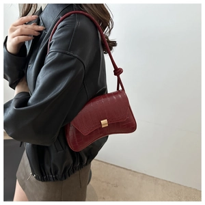 Detail view of burgundy crocodile pattern crossbody bag with golden buckle on model