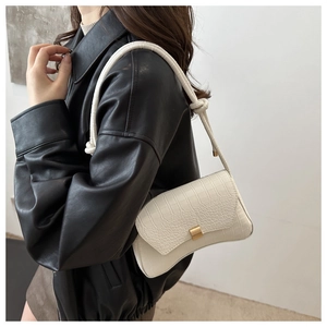 Detail of white crocodile pattern shoulder bag with gold clasp and woven strap