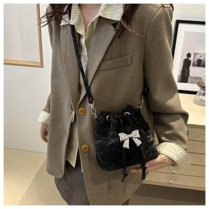 Detail of black pleated bucket bag with silver bow ornament worn on beige blazer