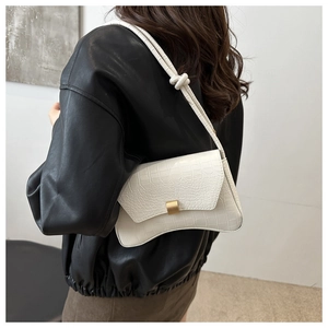 Close-up of white crocodile pattern shoulder bag with matte gold buckle on black leather jacket