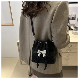 Detail of a black velvet bucket bag featuring a silver bow and adjustable shoulder strap