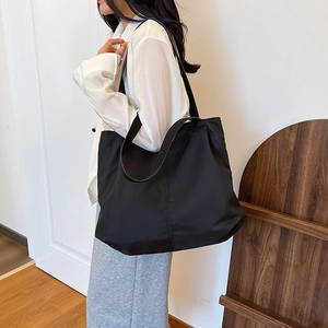 Close-up of a large black minimalist canvas tote bag carried over the shoulder by a model