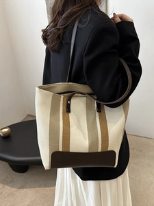 Detail of striped canvas tote bag with brown leather corner reinforcements and handles