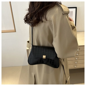 Detail view of black crocodile pattern crossbody bag with golden buckle on a trench coat