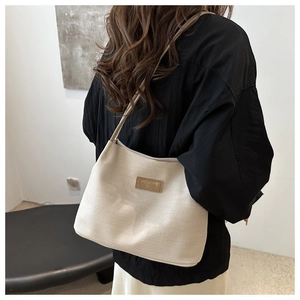 Détail du sac cabas beige gaufré avec logo en cuir marron et fine bandoulière élégante
