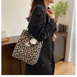 Detail of leopard print canvas tote bag with black strap and white plush pendant accessory