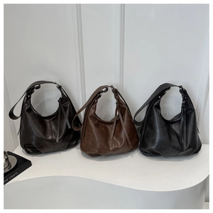 Three minimalist soft leather tote bags in black, brown, and grey on geometric stands