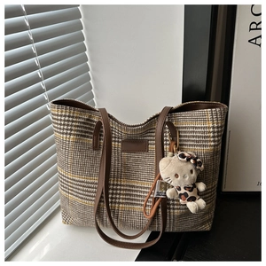 Detail der Vintage-Karo-Canvas-Tragetasche mit braunen Ledergriffen und Leoparden-Kitty-Anhänger