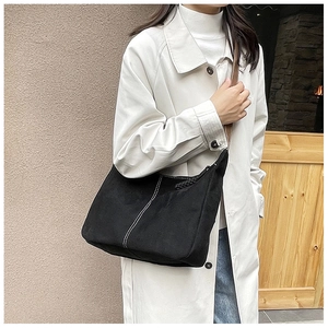 Détail d'un sac cabas en toile noire avec coutures blanches et lanières en cuir marron