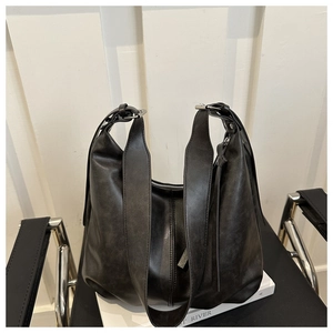 Detail view of vintage black leather hobo bag on a white book with broad shoulder strap