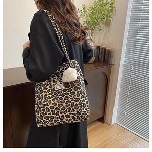 Detail of leopard print canvas tote bag with plush charm and woven brand label