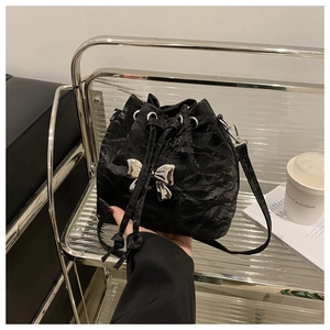 Close-up of black pleated bucket bag featuring a metallic silver bow and drawstring detail