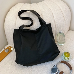 Large black minimalist nylon tote bag shown in a cozy lifestyle setting on a soft sofa