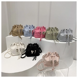 Detail showing various colors of drawstring bucket bags with metal bow buckle on white stands