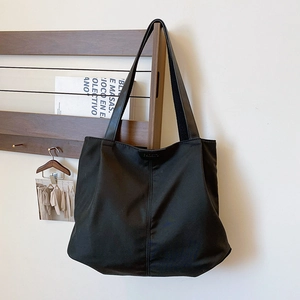 Detail of black nylon tote bag with vertical stitching and leather label on wooden rack
