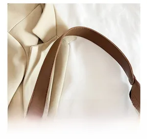 Detail of a brown leather shoulder strap with neat stitching on a beige blazer background