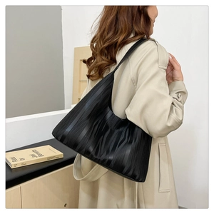 Detail of black wave-textured leather tote bag worn with a beige trench coat