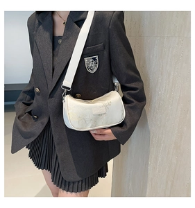 Close-up of beige crossbody bag with delicate floral embroidery and wide fabric strap