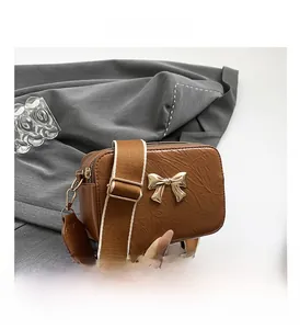 Detail of brown pleated PU crossbody bag featuring a golden metal bow and wide strap