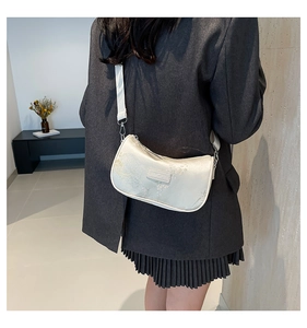 Detailed embroidery on the cream crescent shoulder bag worn by model in minimalist setting