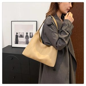 Close-up of a large tan hobo shoulder bag worn with a grey trench coat in a home setting