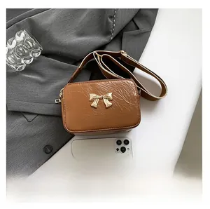 Brown leather crossbody bag with golden bow buckle and phone for size reference