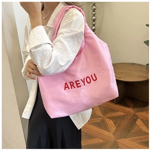 Grand sac cabas rose avec lettrage rouge porté par un mannequin dans un décor épuré