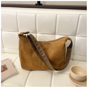 Sac hobo en daim marron avec large bandoulière en cuir sur un canapé blanc style vintage