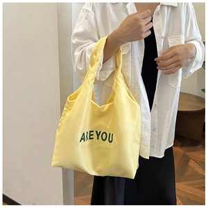Détail du sac cabas en nylon jaune avec imprimé lettré noir tenu dans un cadre chaleureux