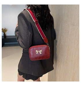 Detail of red crossbody bag featuring gold bow buckle and wide woven shoulder strap