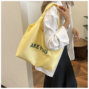 Détail d'un sac cabas en toile jaune avec lettrage ARE YOU et de longues bandoulières