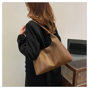 Detail view of brown leather tote bag with wavy texture on shoulder of a model