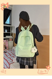 Detailed back view of green canvas backpack with floral embroidery and bear charm