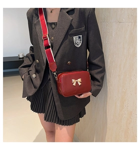 Detail of red crossbody bag featuring a golden bow and wide striped shoulder strap