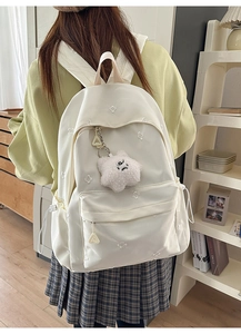 Detail of white school backpack with flower embroidery and a plush cloud charm