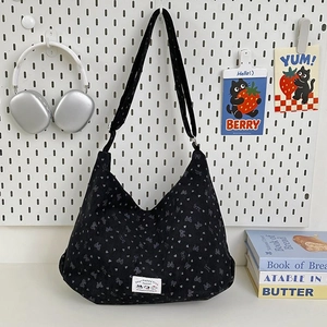 Close-up of black corduroy shoulder bag featuring grey bow prints and woven brand label