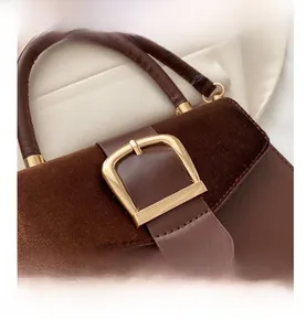 Close-up of brown velvet and leather stitching detail with gold metal buckle on handbag