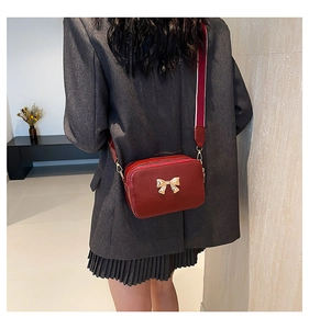 Detail view of red faux leather crossbody bag with golden bow buckle and wide strap