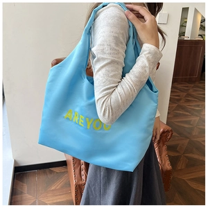 Détail du sac cabas bleu avec lettrage jaune posé sur un siège en cuir