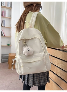 Detail of sweet floral embroidery and plush star pendant on beige school backpack