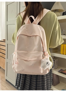 Detailed close-up of pink school backpack featuring white floral embroidery and a bear charm