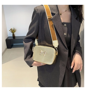 Detail of golden metallic crossbody bag with bow buckle and wide brown strap