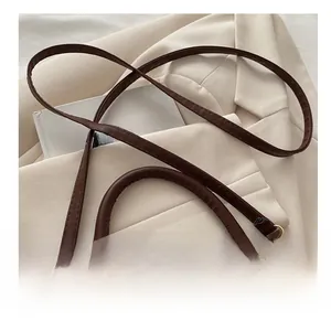 Detail of a brown leather and velvet crossbody bag with golden hardware on a white blazer