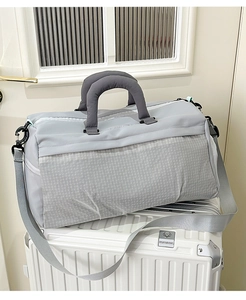 Close-up of light grey gym bag with tear-resistant fabric resting on a white suitcase