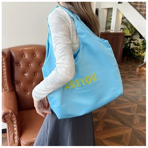 Grand sac cabas bleu clair avec lettres jaunes porté à l'épaule par un mannequin en studio