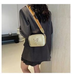 Detail of golden metallic crossbody bag with bow decoration and wide fabric shoulder strap