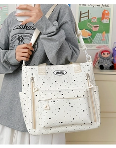 Dettaglio borsa shopper bianca con stelle, tasche a zip e tracolla in tessuto beige