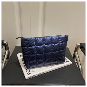 Close-up of dark blue quilted handbag with metallic glossy finish and zipper detail