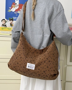 Detail of a brown corduroy crossbody bag with black hearts and woven logo tag
