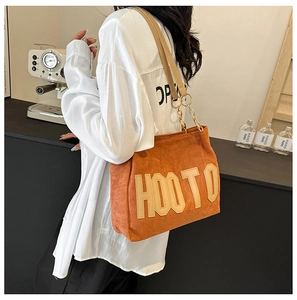 Détail du sac cabas en daim orange avec grand lettrage et bandoulière en chaîne dorée
